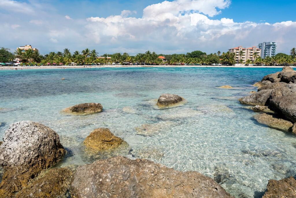 Dramatic image of the Caribbean coast of Juan Dolio, Dominican Republic with large rocks in the foreground of the bay and beach on the horizon.