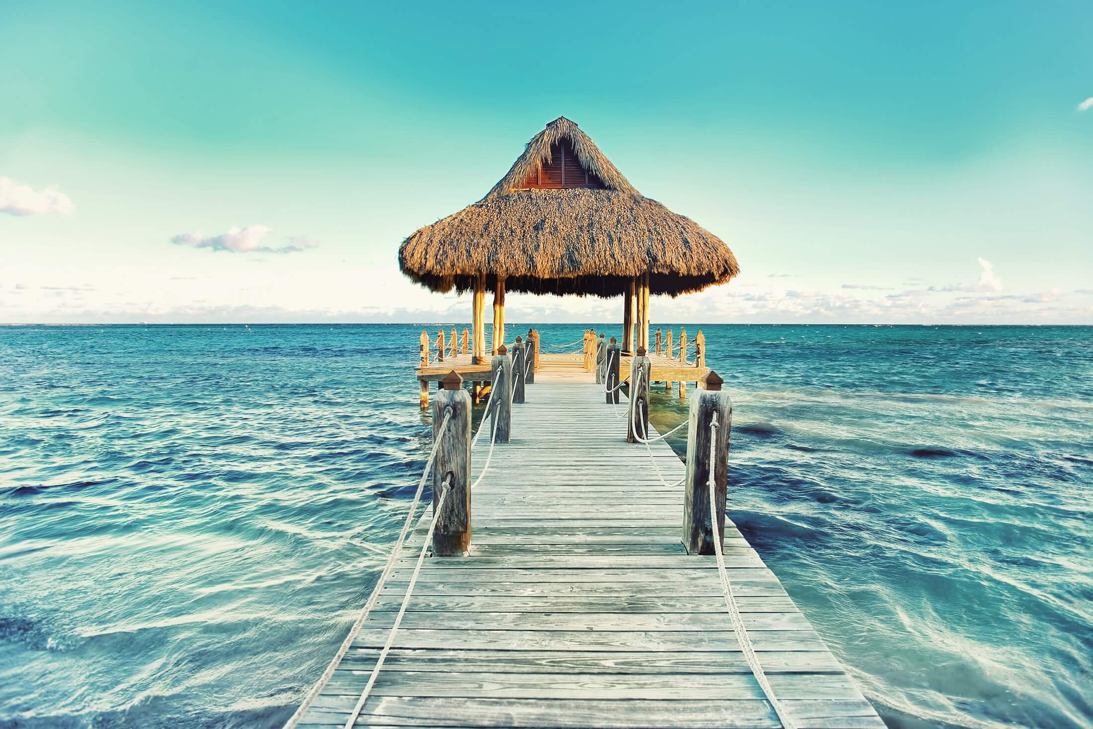 Tropical white sandy beach. Palm leaf roofed wooden pier with gazebo on the beach. Punta Cana, Dominican Republic. Instagram filter