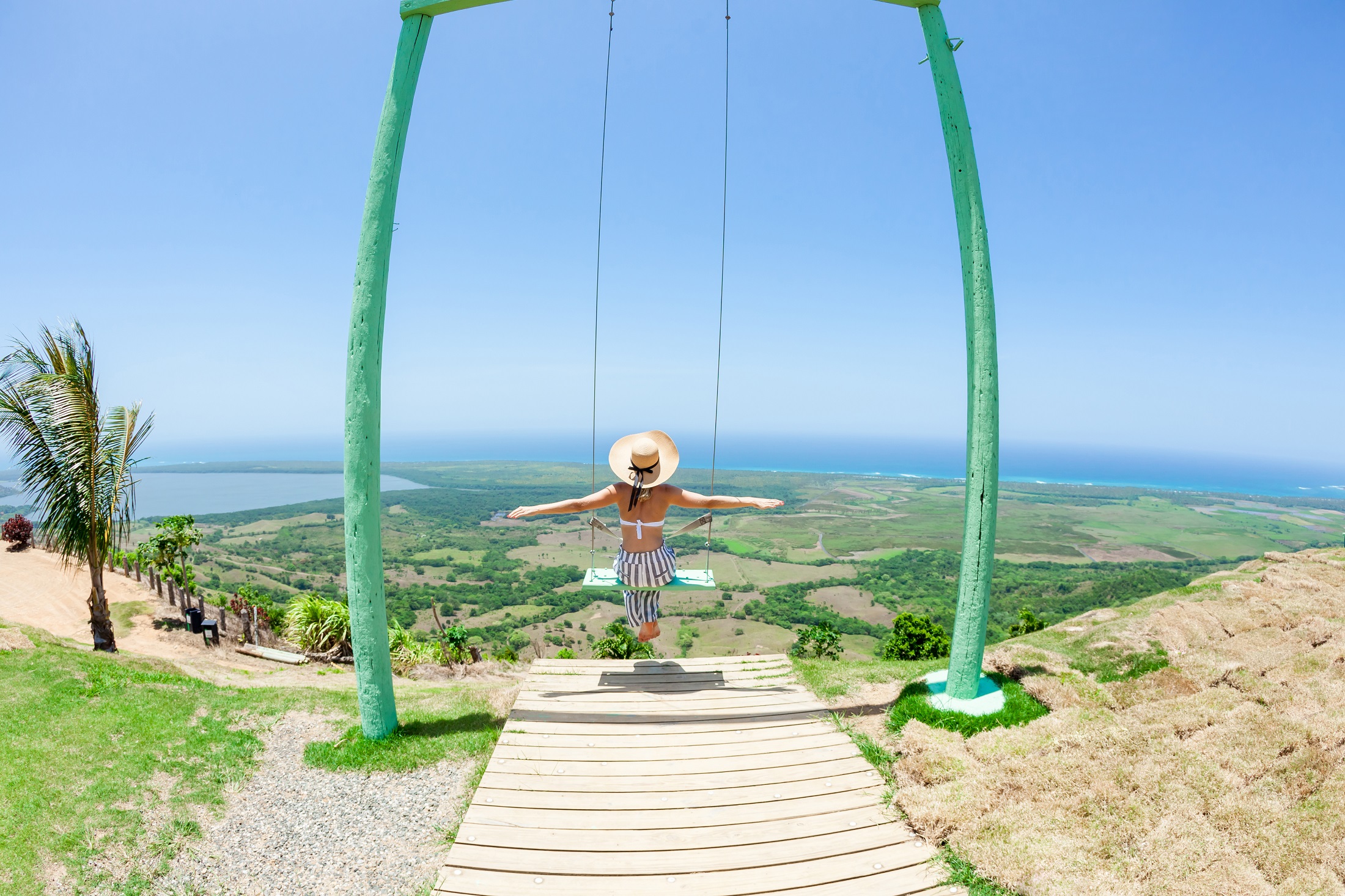Woman swinging on swings over the green mountains with ocean sea caribbean tropical landscape and horizon line with blue sky. Montana Redonda, Dominican republic. Freedom concept. Touristic place