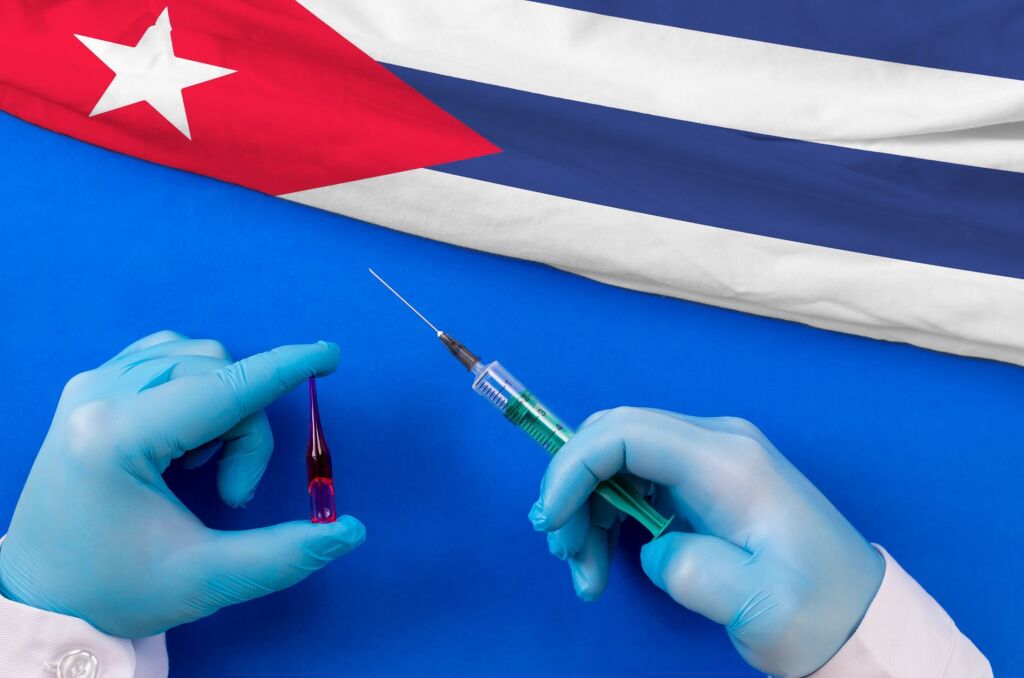 Cuba Vaccination. Hands of doctor holding syringe and coronavirus (COVID-19) vial vaccine on flag Cuba