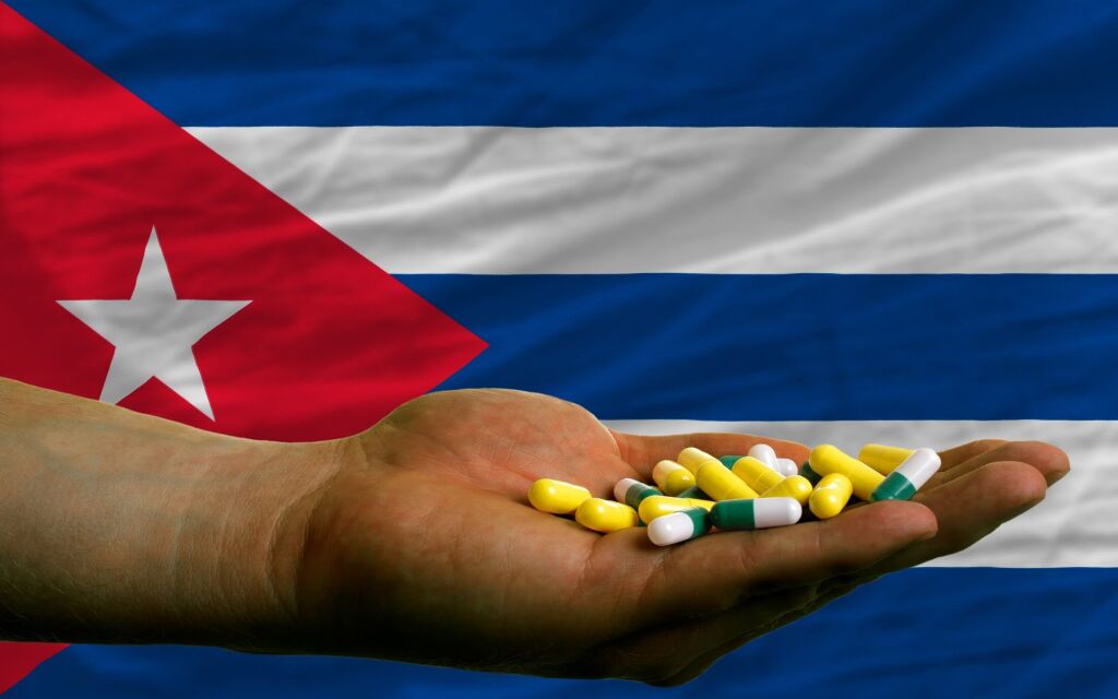 man holding capsules in front of complete wavy national flag of cuba symbolizing health, medicine, cure, vitamines and healthy life