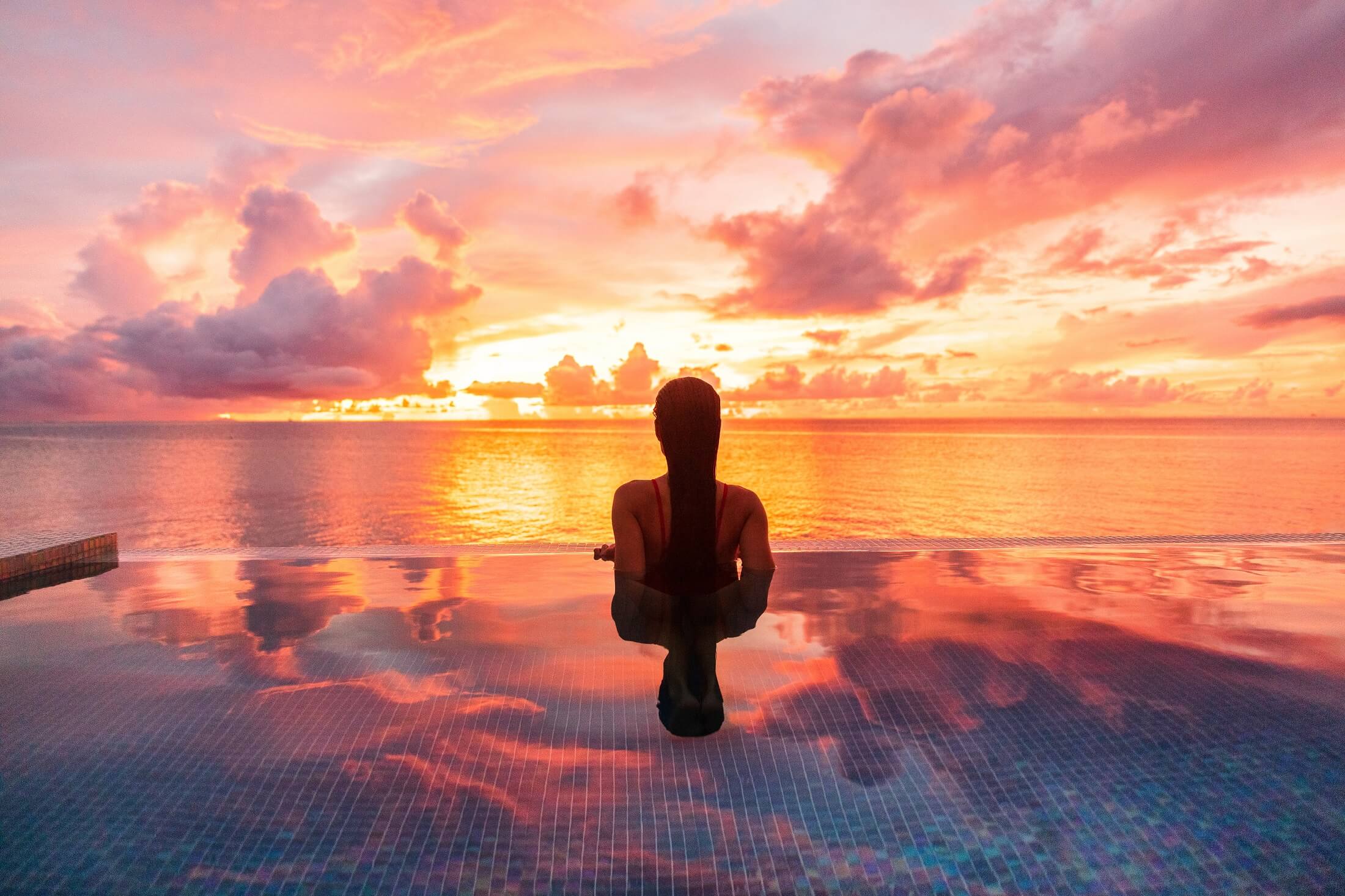Paradise luksusowy ośrodek miodowy wypad miejsce na idylliczne Karaiby tropikalny krajobraz hotelu, kobieta sylwetka pływanie w basenie bez krawędzi oglądania zachodu słońca spokojny. Zimowy wypad o zmierzchu.