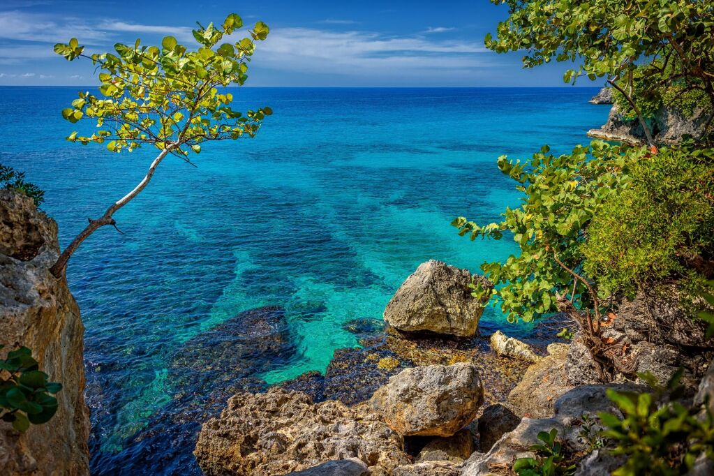 Piękna turkusowa i niebieska woda w pobliżu skał i klifów w Negril na Jamajce. Drzewo po lewej i skały po prawej z piękną laguną w morzu
