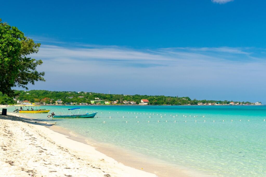 Słoneczny dzień wzdłuż plaży Seven Mile w tropikalnym Negril na Jamajce. Łodzie turystyczne czekają na pasażerów i kaukaskich turystów w wodzie na odległość. Karaiby Jamajki letnie wakacje na plaży.