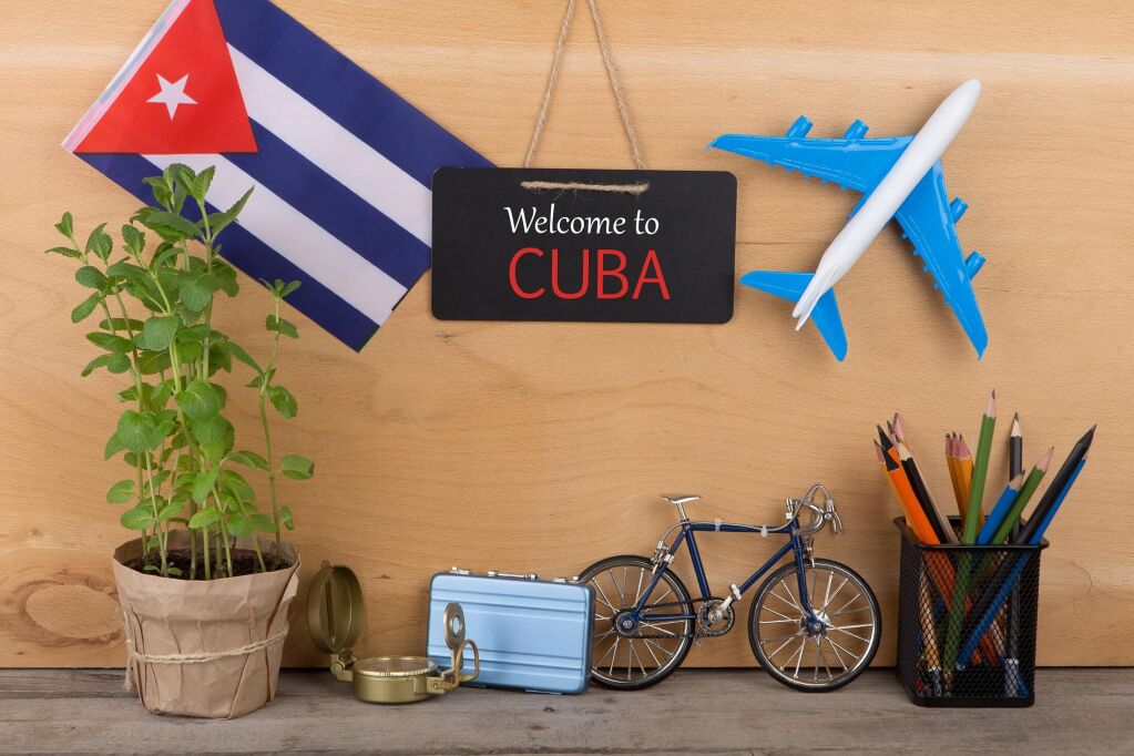 Travel time - blackboard with text "Welcome to Cuba", flag of the Cuba, airplane model, camera, bicycle on brown wooden background