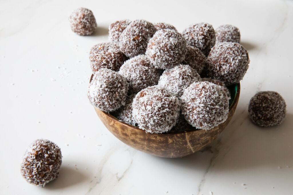 Delicious Coconut-Chocolate balls covered with grated coconut served in a coconut plate against white background. Copy space. Christmas, Indian burfi treat, healthy energising cookie concept
