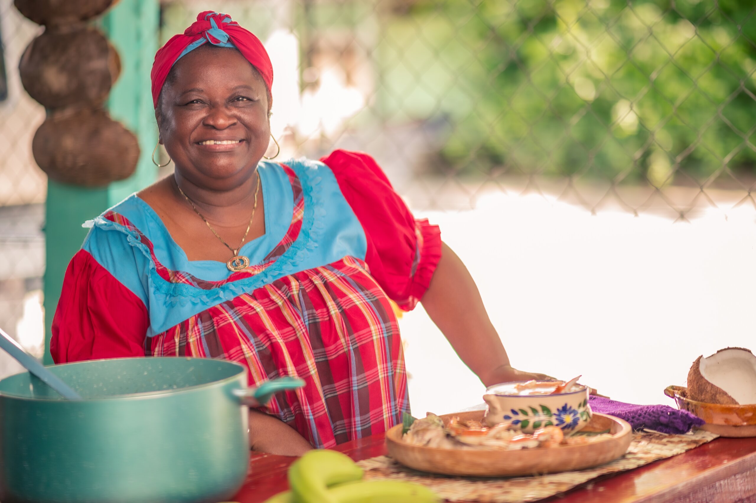 Portrait of an adult woman standing in her kitchen looking at a camera. Proud African American woman in colorful Garifuna dress.
