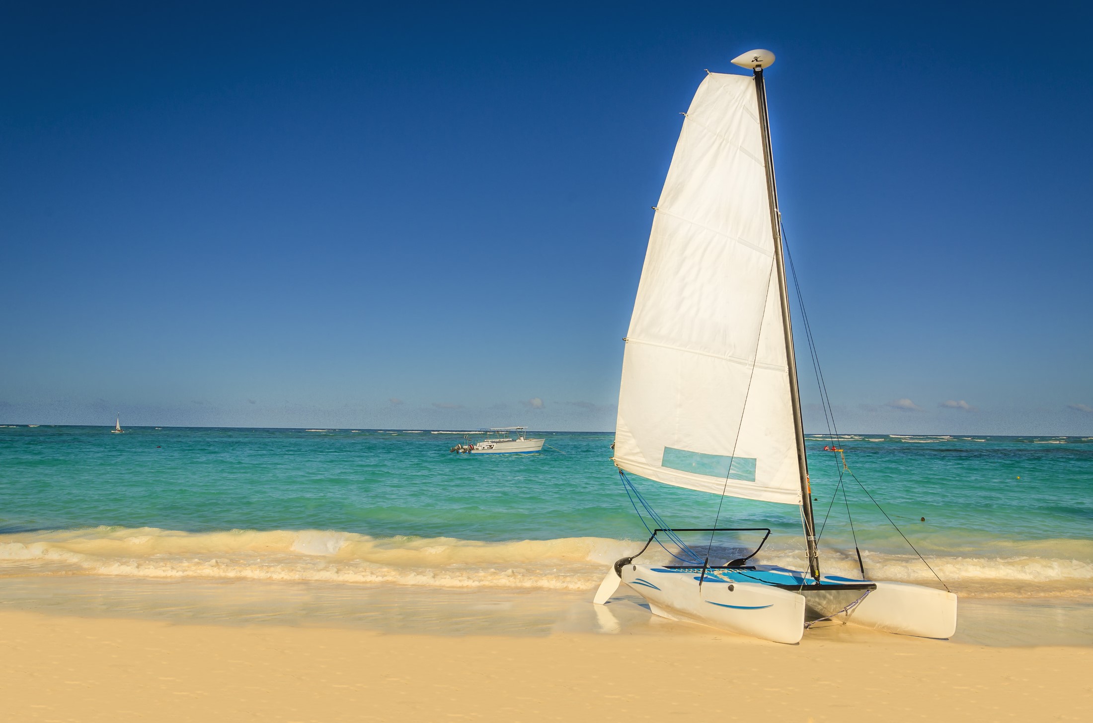 Biały katamaran na egzotycznej karaibskiej plaży na tle złotego piasku, lazurowego oceanu i błękitnego nieba